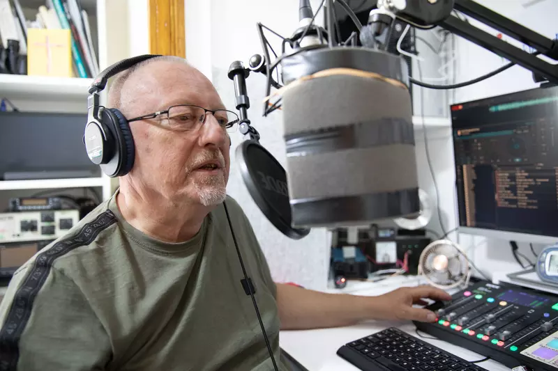 John sits with headphones on, talking into a radio mic