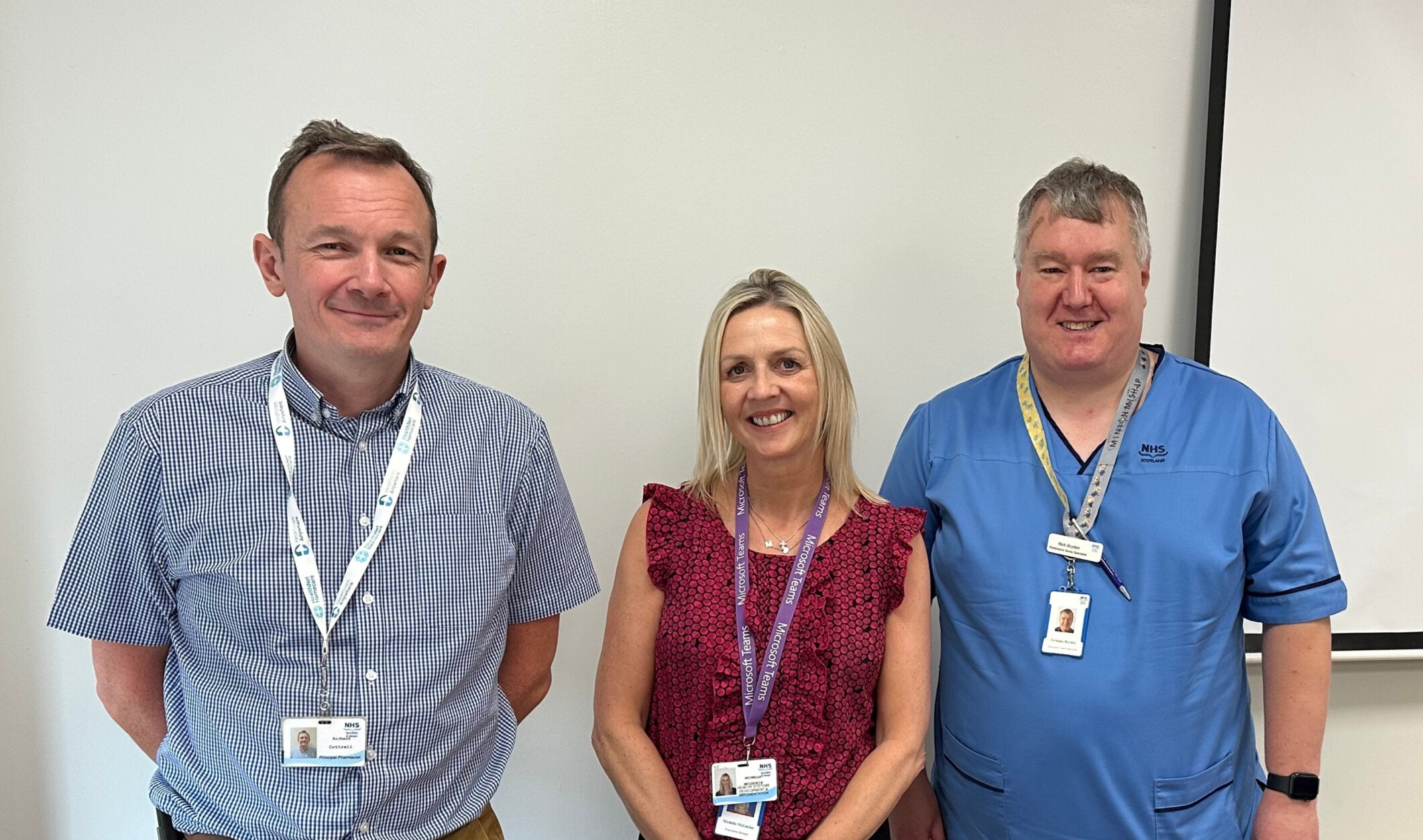 3 members of NHS staff stood in a row smiling.