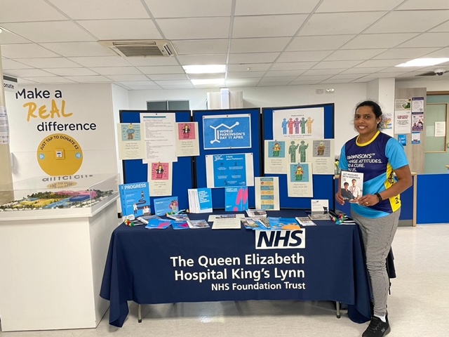 A nurse in a Parkinson's UK t-shirt stands in front of a Parkinson's information stand.