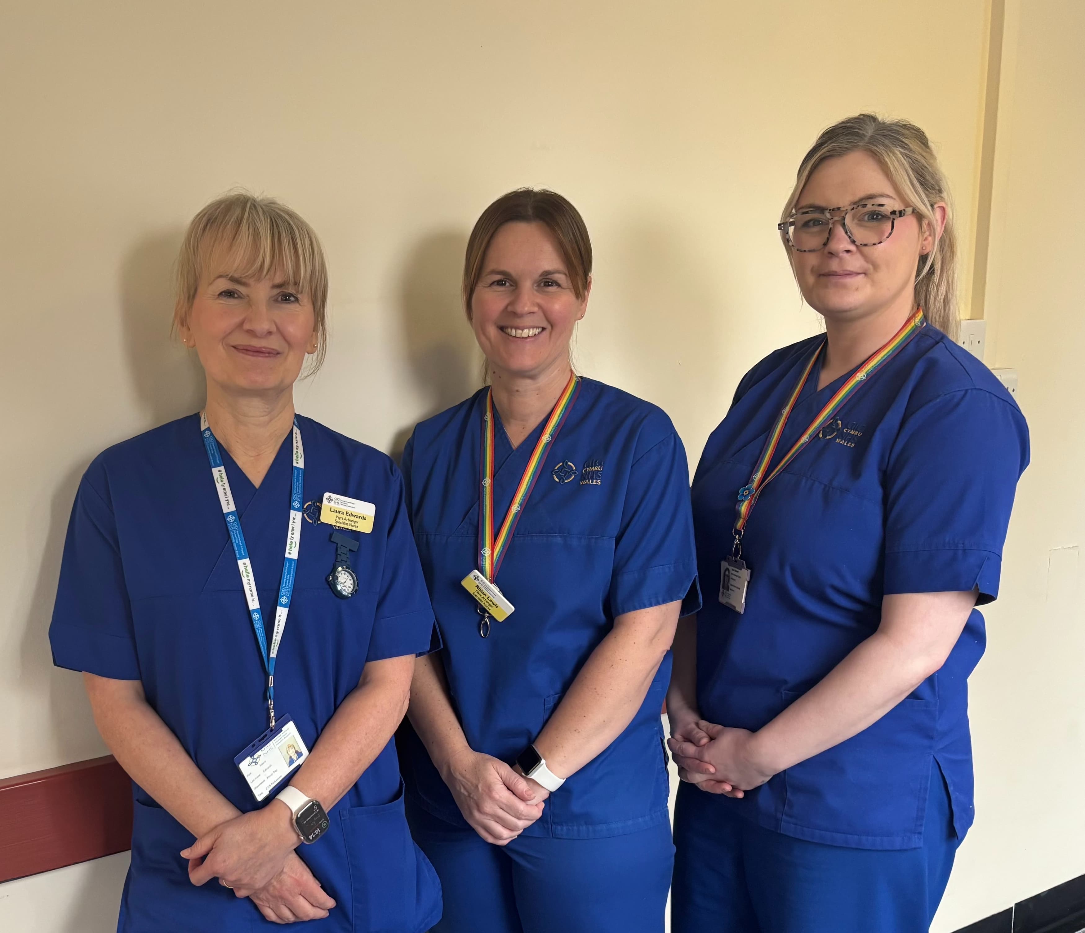 3 female nurses in blue uniforms smile at the camera.