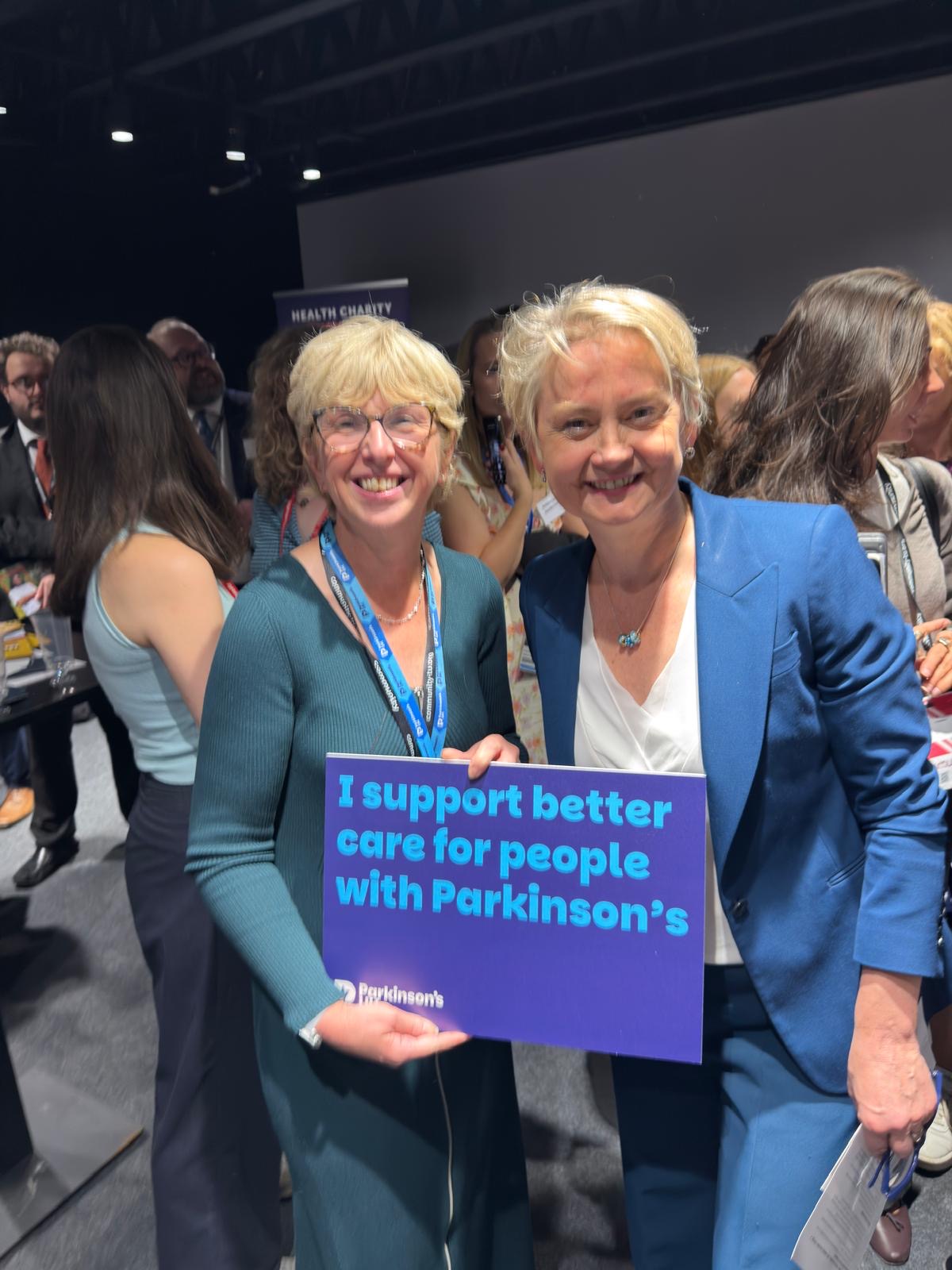Parkinson's UK chief executive and Secretary of State for Health and Care pose for a photo while holding a photoboard stating