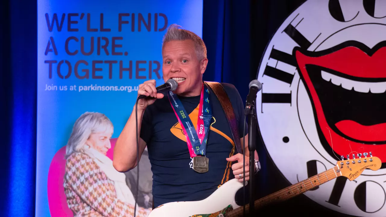 Rob Deering performing on stage with a micropohe and guitar