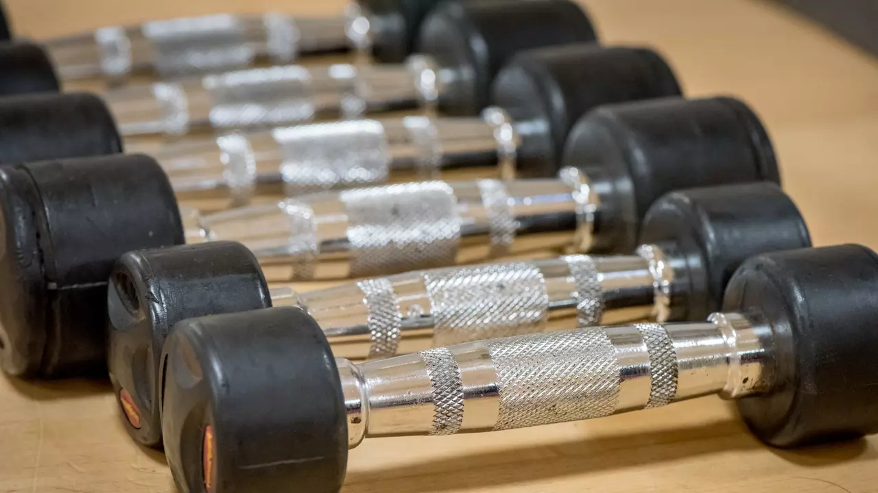 An image of some metal gym weights on a wooden floor. The weights are silver with black rubber handles. 