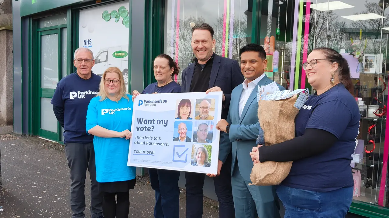 A group of people in Parkinson's UK t-shirts stand with Scottish Conservative leader, Russell Findlay. Together they're holding a sack that says 'Your move! Mail' which is filled with postcards and an oversized postcard that says 'Want my vote? Then let's talk about Parkinson's. Your move!'.