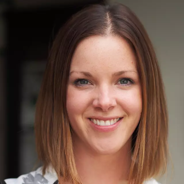 Emma smiling to camera. She has shoulder length brown hair and is wearing a black and white blouse.