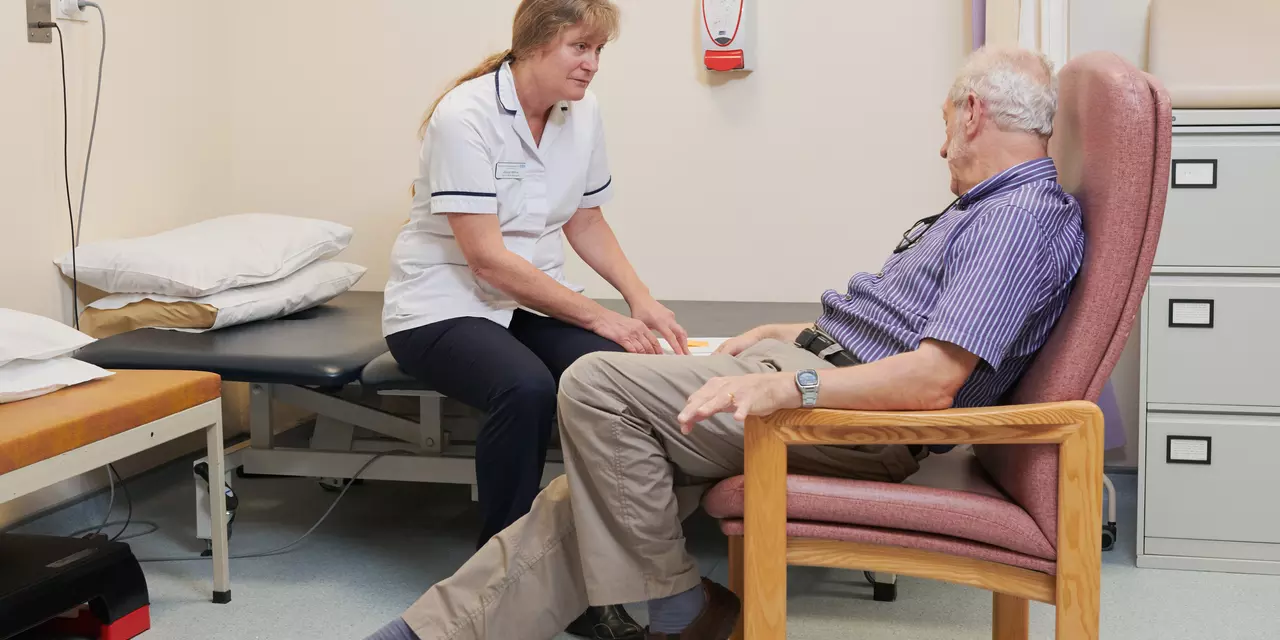 Man sat on a chair, talking to a healthcare professional.