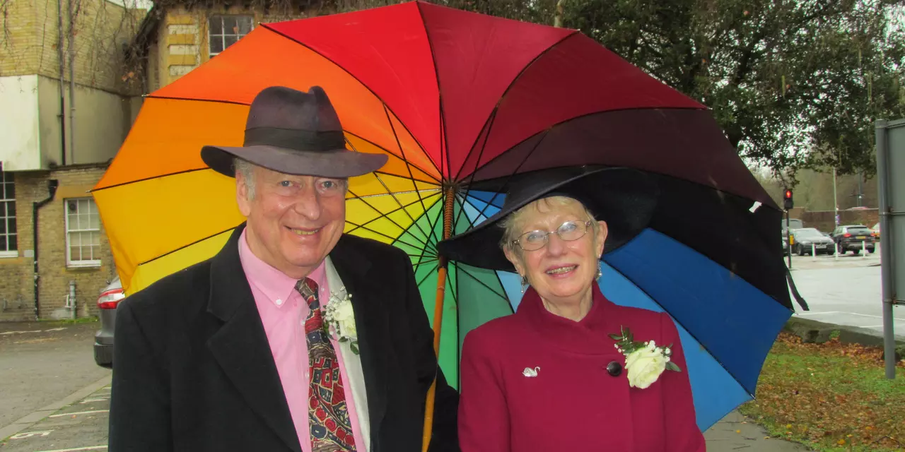Pen and Joss smiling under a colourful umbrella, on their wedding day
