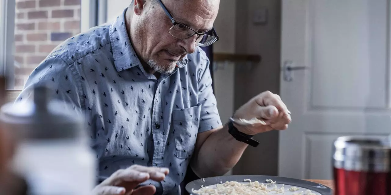 A man struggle to get a fork to his mouth while eating noodles