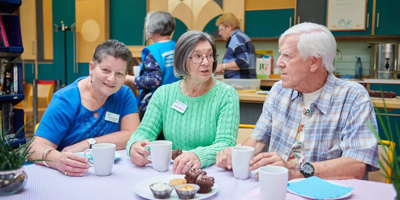 Mariëtte sitting at a table with a man and a woman, enjoying tea and cake