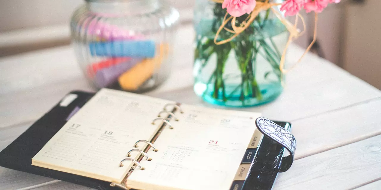 An open diary lying on the table. There is a vase of pink flowers next to it.
