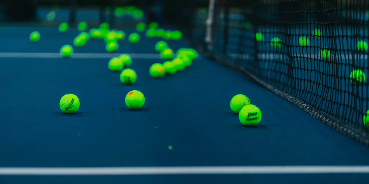 Yellow tennis balls scattered by a net. The tennis court floor is blue.