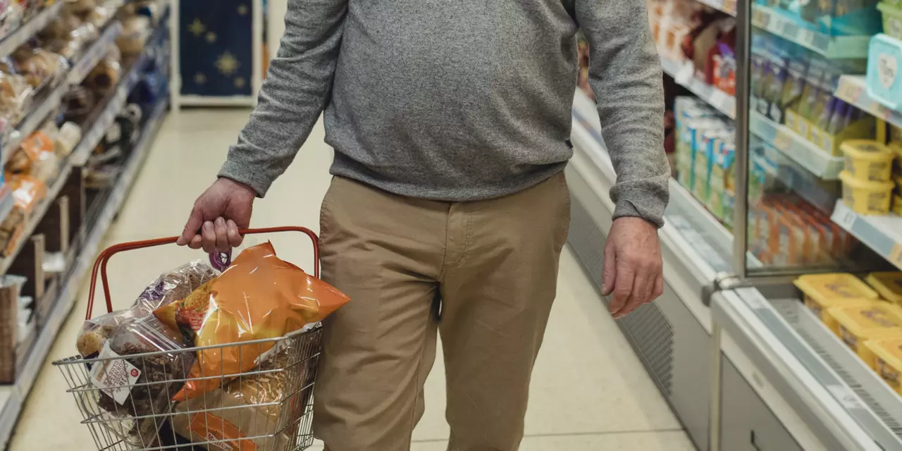 Man holding shopping basket, walking down a supermarket aisle.