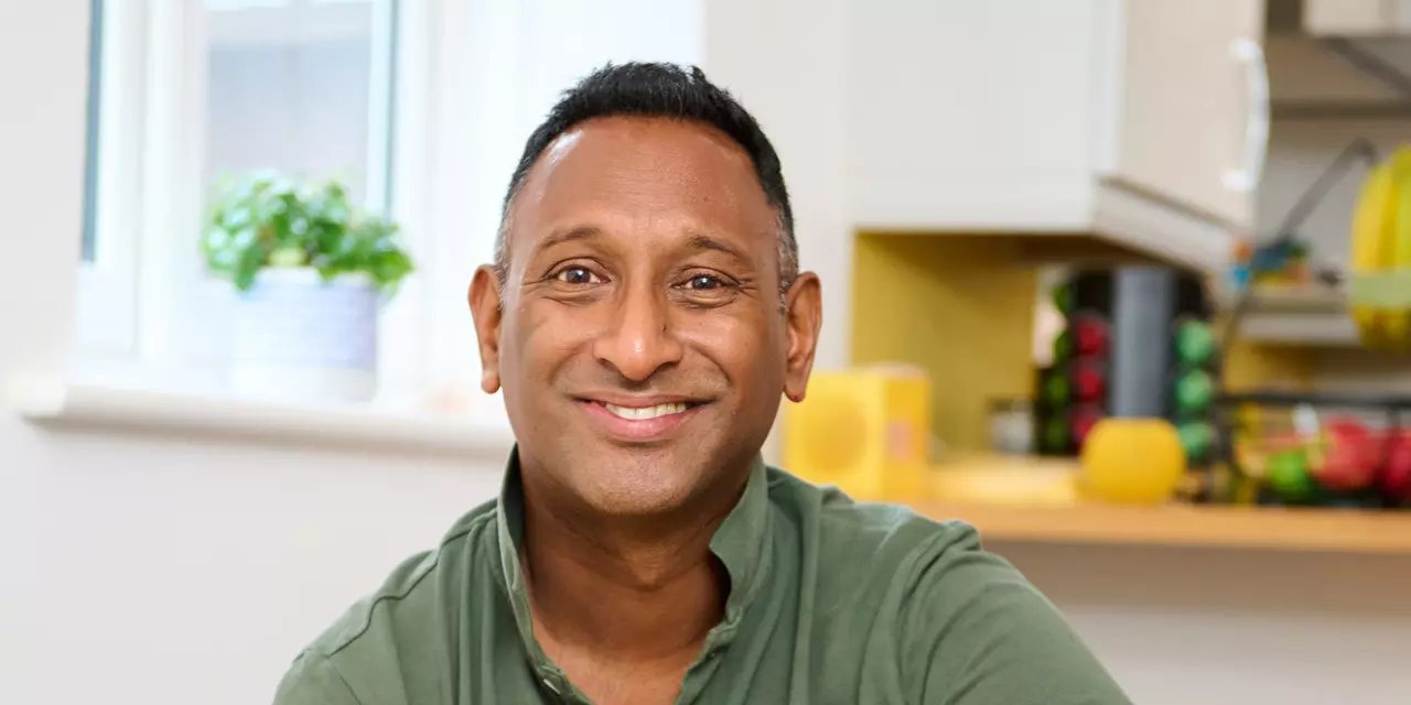 Kuhan smiles at the camera. He is in his kitchen and wears a dark green polo tshirt.