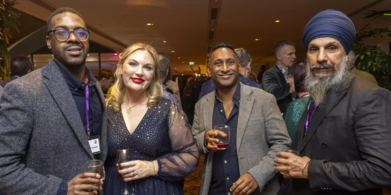 Four people smartly dressed holding glasses at event