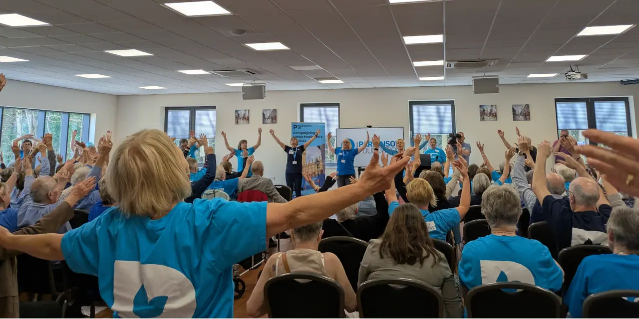 A group of people wearing blue t-shirts raise their arms and sing 
