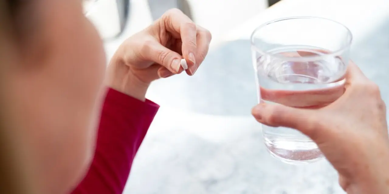 Lady sat at a table with pill in hand and a glass of water