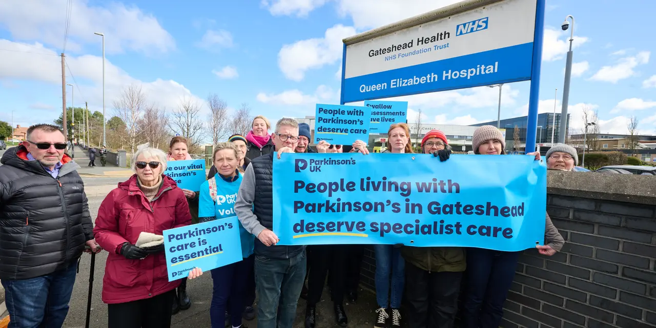 A group of people stand outside Queen Elizabeth hospital in Gateshead while holding a banner and boards