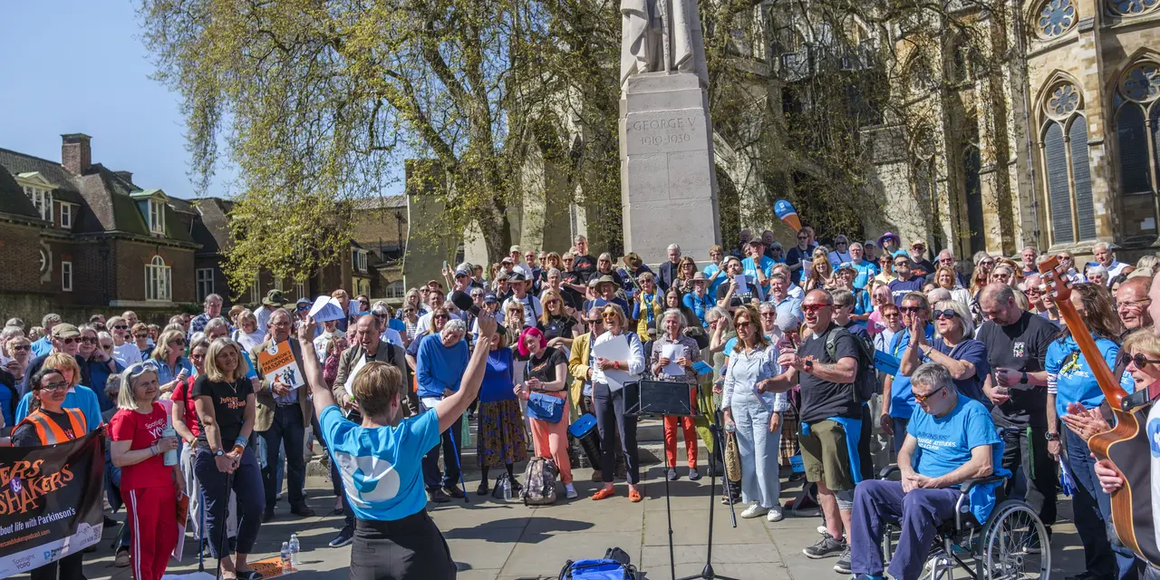 A large group of people stand outside and sing together