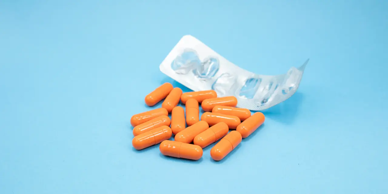 An empty blister pack with orange pills next to it against a light blue background
