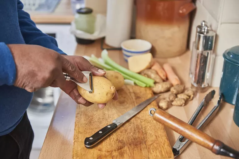 A man's hand peeling potatoes in his kitchen