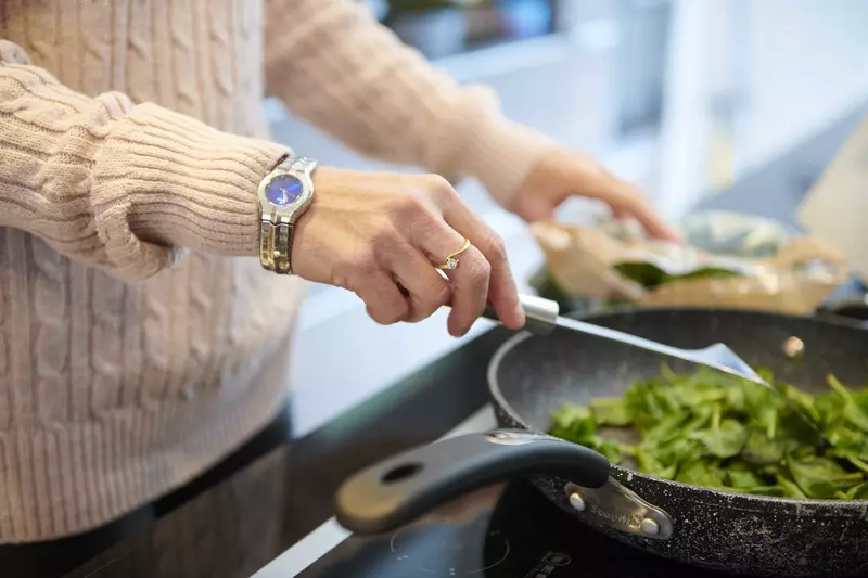 Hand stirring a frying pan of spinach