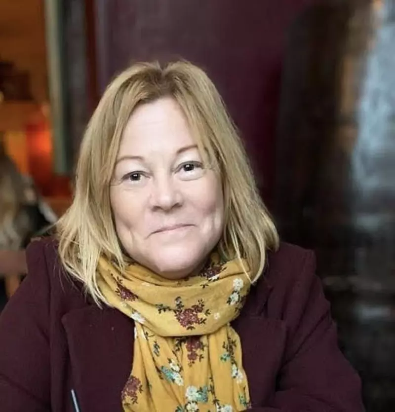 Leah smiling at the camera. She has shoulder-length blonde hair. She is wearing a mustard yellow scarf and a maroon jacket.