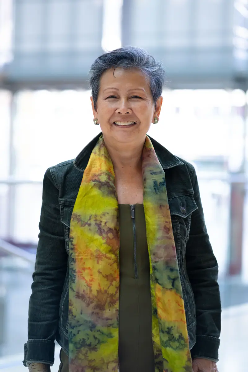 Carroll, wearing a green jacket and a patterned yellow and green silk scarf